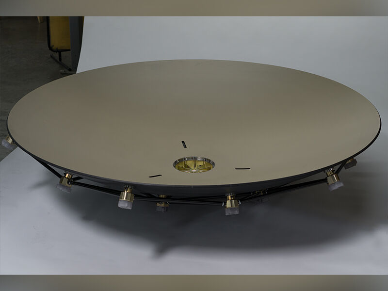 Finished deformable reflector laying on a white paper surface for photography. The interior of the dish is painted a tan color, and the backing structure is visible, including attached nodes and connecting carbon fiber tubes.